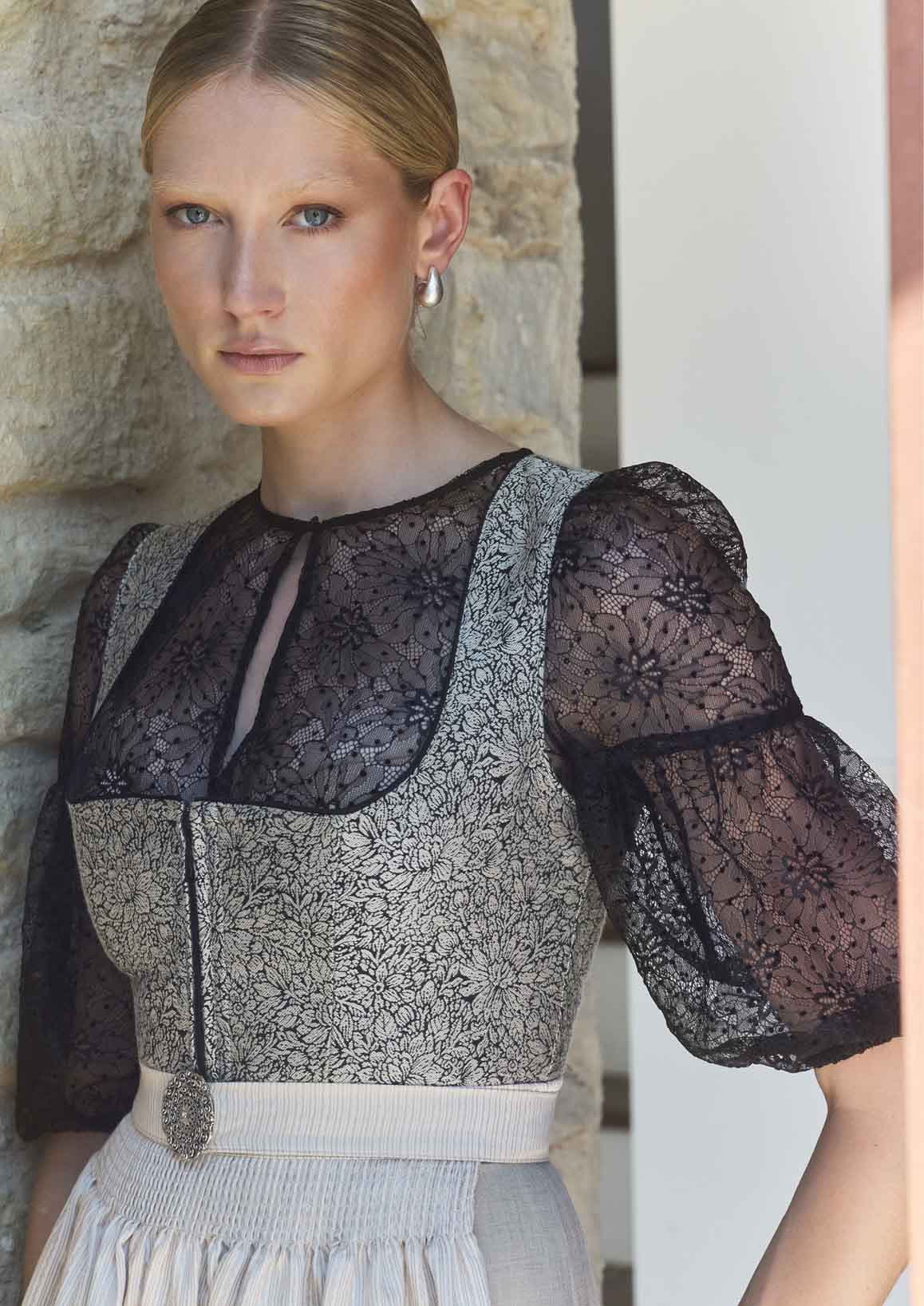 Frau trägt ein graues Dirndl und einer hochgeschlossenen schwarzen Dirndlbluse.