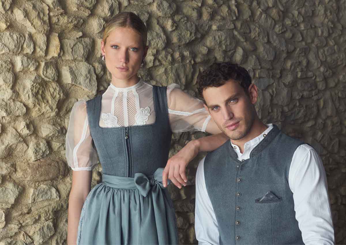 Frau trägt blaues Dirndl mit Spitzen-Dirndlbluse und Herr trägt passende blaue Weste mit weißem Hemd.